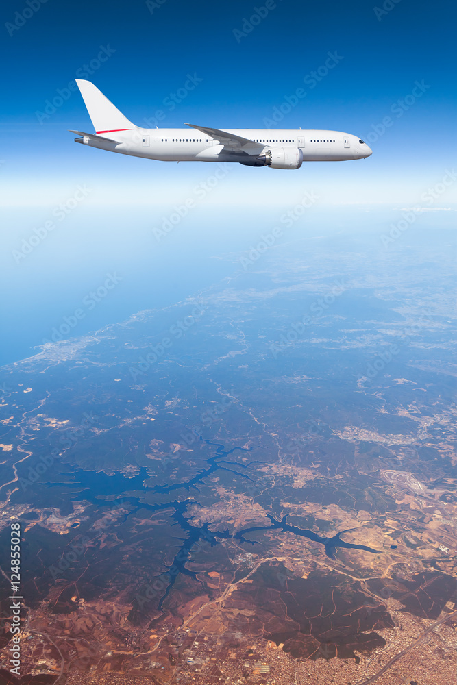Podróż samolotem, samolot lecący w błękitnym niebie wysoko nad ziemią - obrazy, fototapety, plakaty 