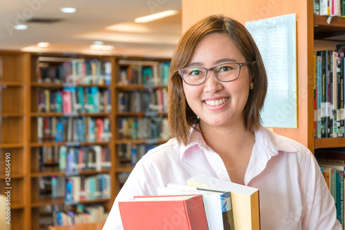 In the library - Aisian female student with books working in a u