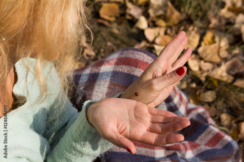 Fototapeta premium Girl sitting on the grass and sees a ladybird.