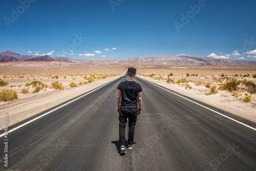 Young man walking alone through an empty street in the desert of Death Valley 
