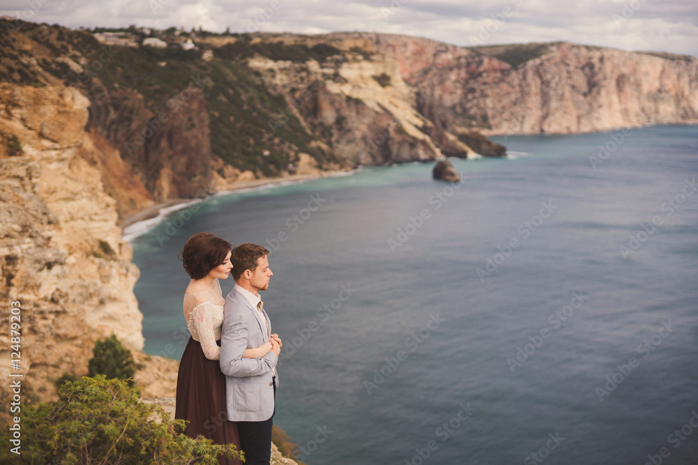 Naklejka premium Romantic and stylish caucasian couple standing on the background of spectacular sea view. Love, relationships, romance, happiness concept.