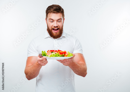 Cheerful young bearded man holding plate with fresh salad