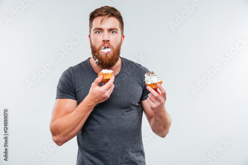 Filthy bearded young man eating cream cakes