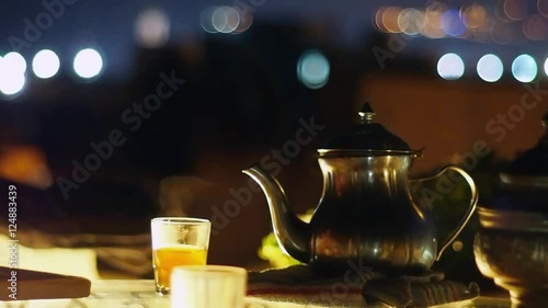 Traditional Metal Pot and Glasses With Steaming Moroccan Tea on the Night City View Rooftop Terrace, Midshot, Night Light