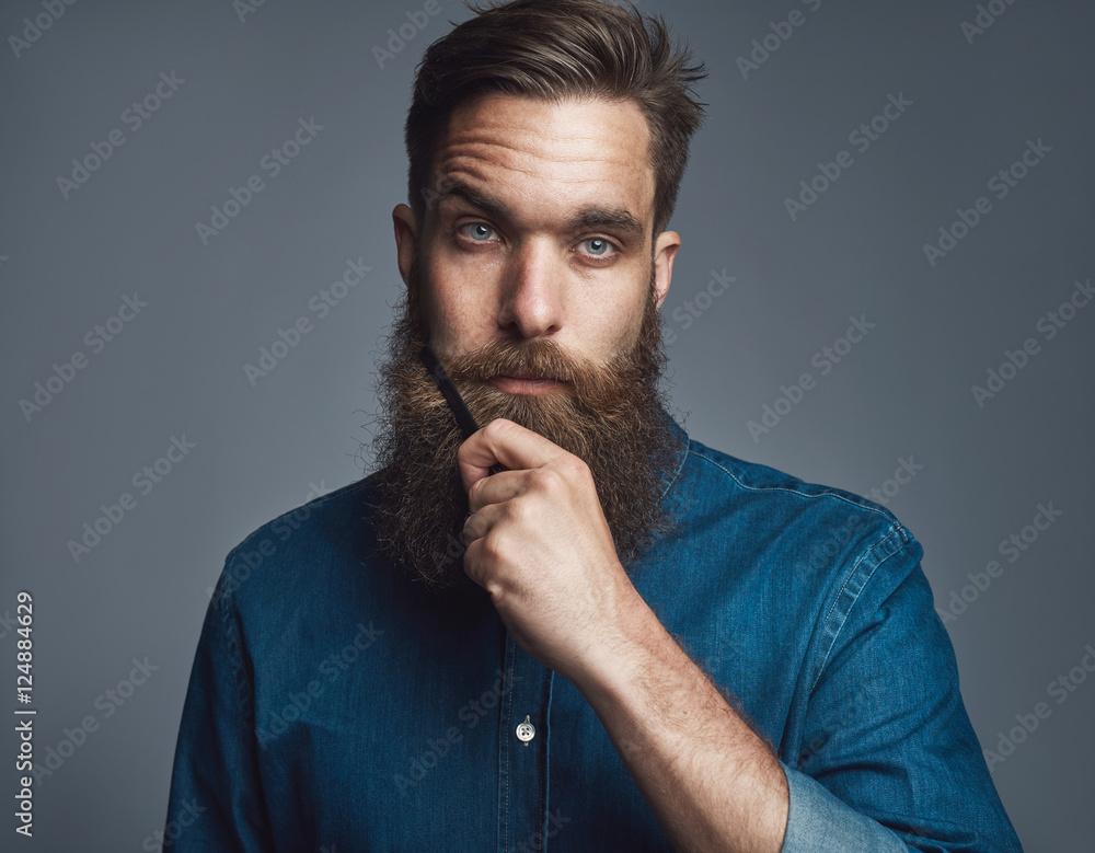 Young man holding his beard with blank stare Young man holding his beard with blank stare