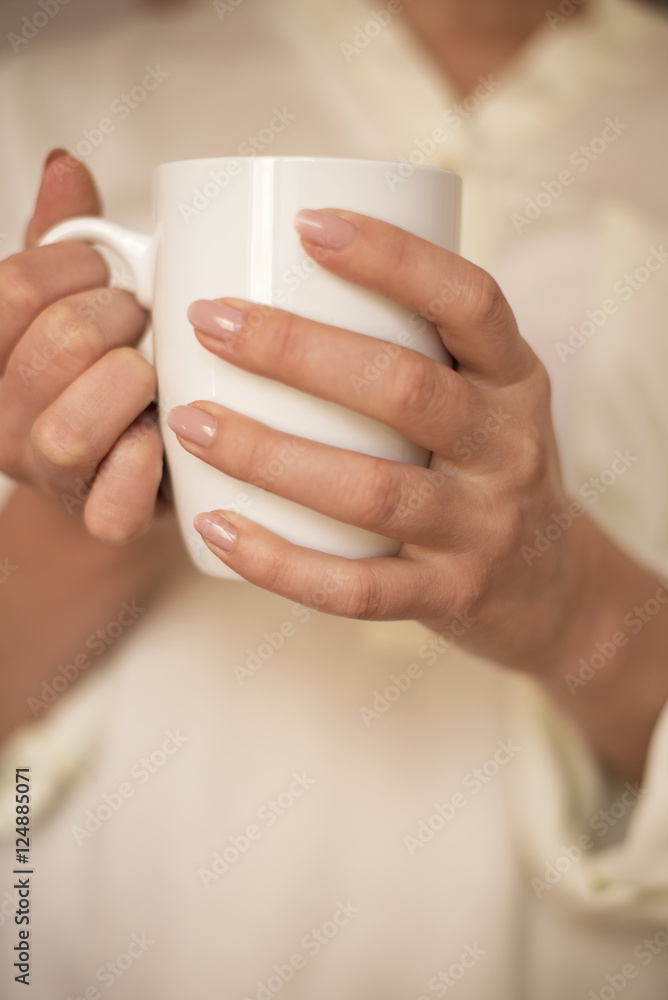 Girl is holding white cup in hands. White mug for woman, gift. Female hands holding hot cup of coffee or tea in morning. Selective focus Girl is holding white cup in hands. White mug for woman, gift. Female hands holding hot cup of coffee or tea in morning. Selective focus