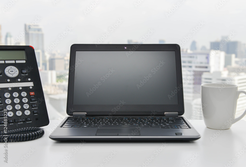 Laptop, IP Phone and coffee cup are on the white table in the office Laptop, IP Phone and coffee cup are on the white table in the office