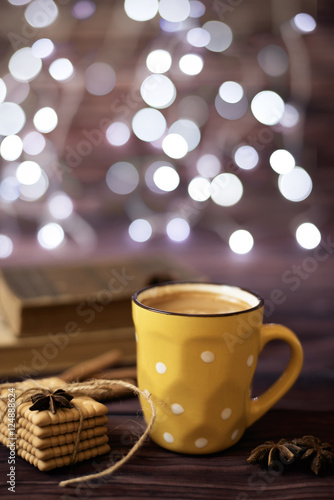 Mug of coffee, cookies, star anise, cinnamon, old books. Blurred lights, wooden background. Winter time, Rustic background with beautiful Christmas lights of bokeh.