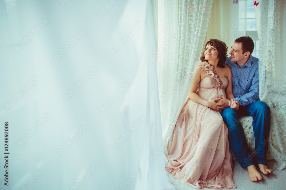 Man in blue and expecting woman in pastel pink dress sit on the Man in blue and expecting woman in pastel pink dress sit on the