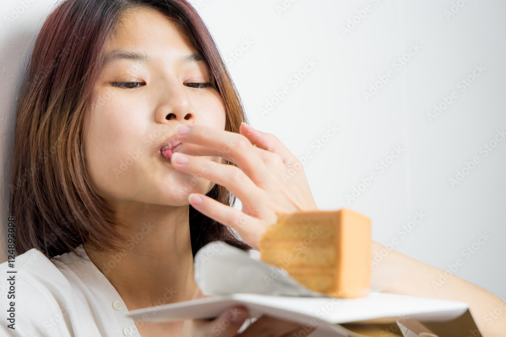 Japanese girl eating cake using her hand. Asian girl licking finger to eat  an orange cake.