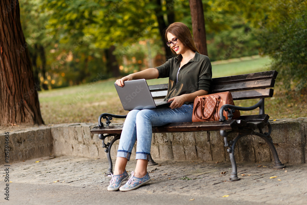 Young female student sitting on a bench in park, she is working on laptop. Young female student sitting on a bench in park, she is working on laptop.