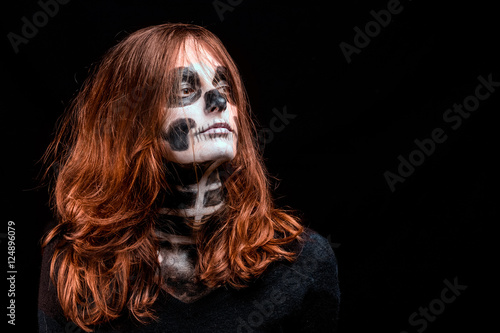 Une femme aux cheveux roux vifs et maquillée en squelette pose sur fond noir