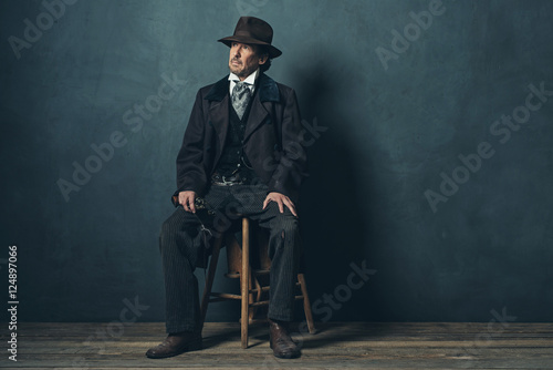 Vintage 1900 western mature man with revolver sitting on wooden photo