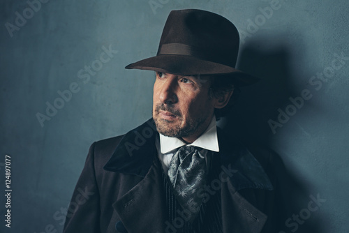 Vintage mature western man with beard against gray wall.