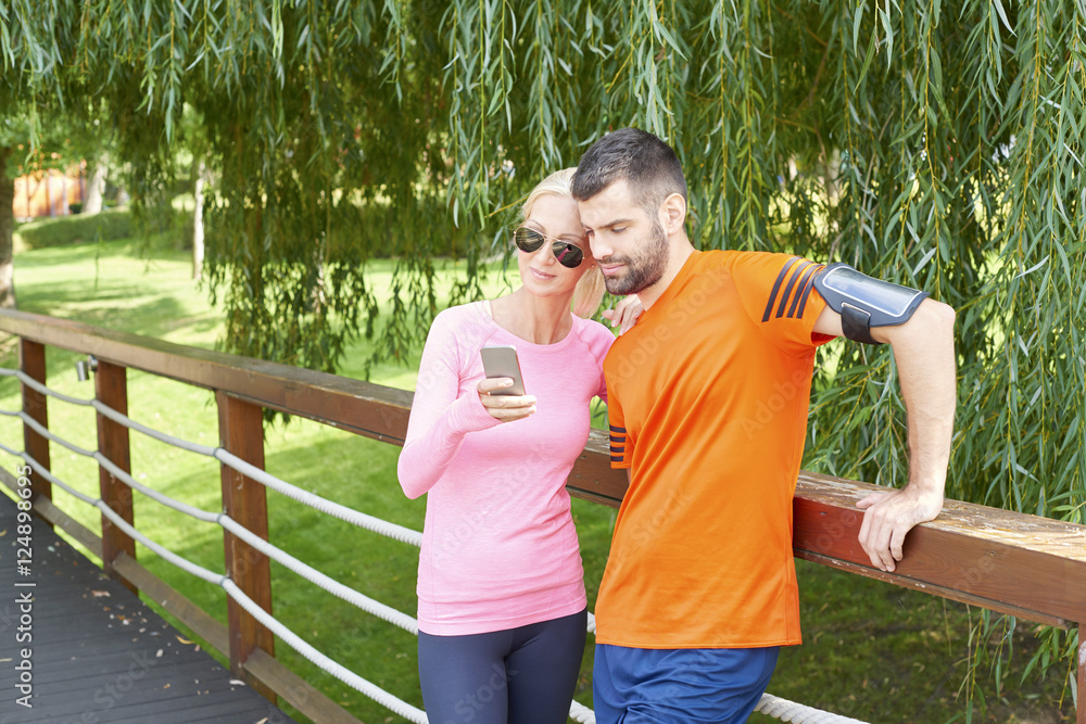 Obraz premium Fit couple after running. Full length shot of a young couple checking runner app on handy after morning workout.