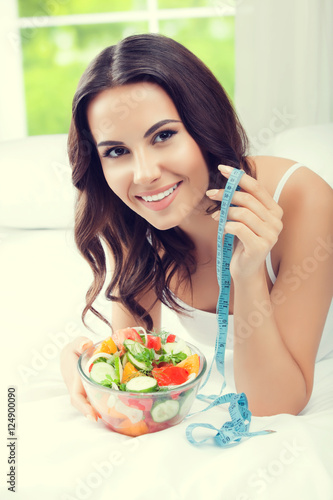 beautiful woman eating salad and measure tape, indoors