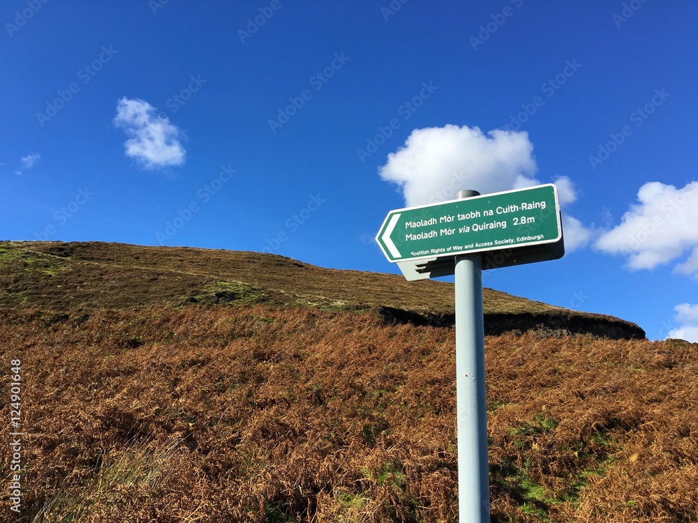 A signpost in both English and Scottish Gaelic points to the footpath for the Quiraing, Isle Of Skye, Scotland, UK. 