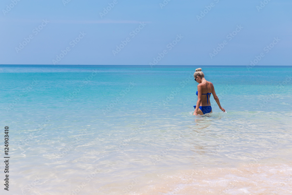 Young pretty slim blonde woman swimming in clear water on tropic