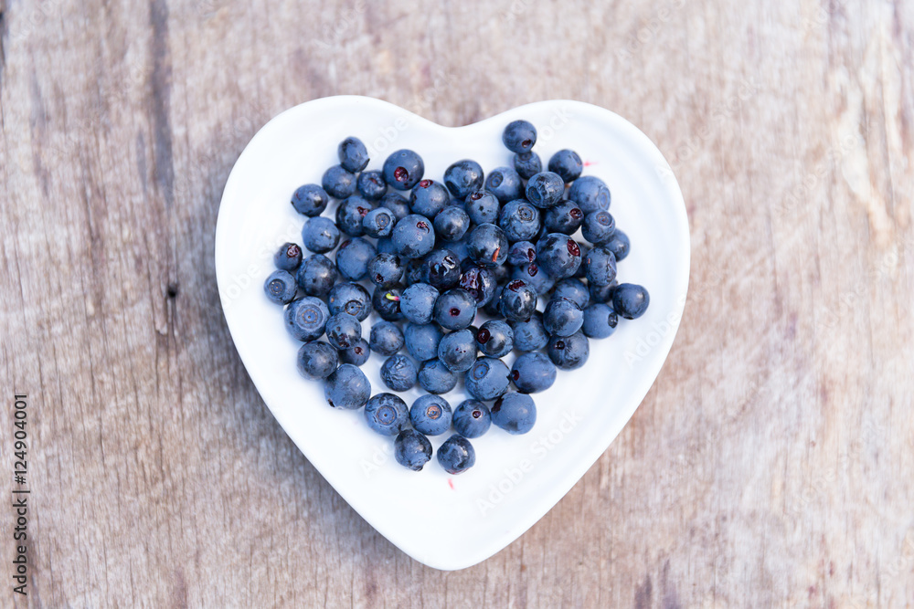 Fresh forest blueberries in heart plate on wooden background autumn Fresh forest blueberries in heart plate on wooden background autumn