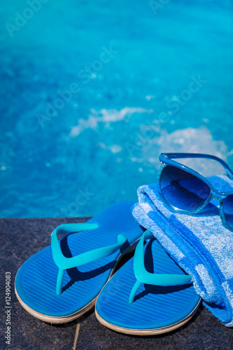 Blue slippers, sunglasses and towel on border of swimming pool