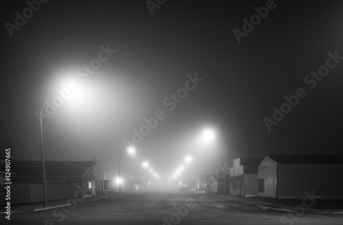 Main street of a small town shrouded in fog under street lights