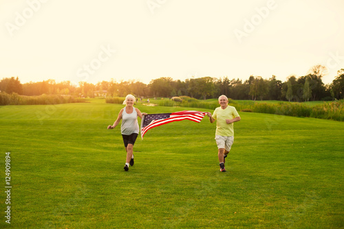 People with American flag running. Smiling senior couple outdoor. Achievements is sports. Former USA athletes.