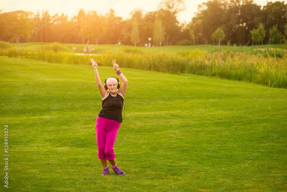 Senior woman in headphones dancing. Lady on grass background. Energy of music. Moving in the rhythm. Senior woman in headphones dancing. Lady on grass background. Energy of music. Moving in the rhythm.