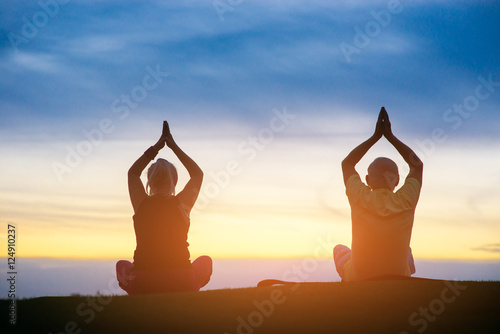 Silhouette of couple doing yoga. People sitting on sunset background. Eternal search of harmony. Mind and body.