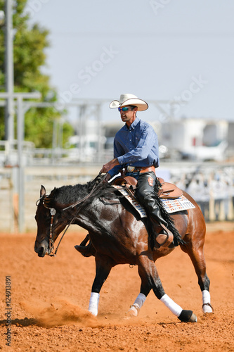 The side view of a rider in cowboy chaps, boots and hat on a horseback running ahead in the dust.