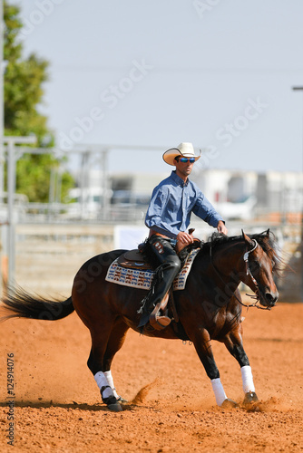 The side view of a rider in cowboy chaps, boots and hat on a horseback performs an exercise during a competition