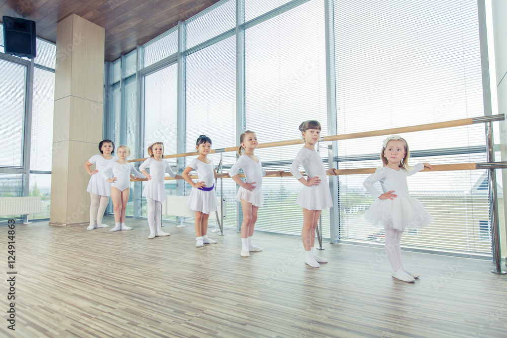 Fototapeta premium Group of seven little ballerinas standing in row and practicing 