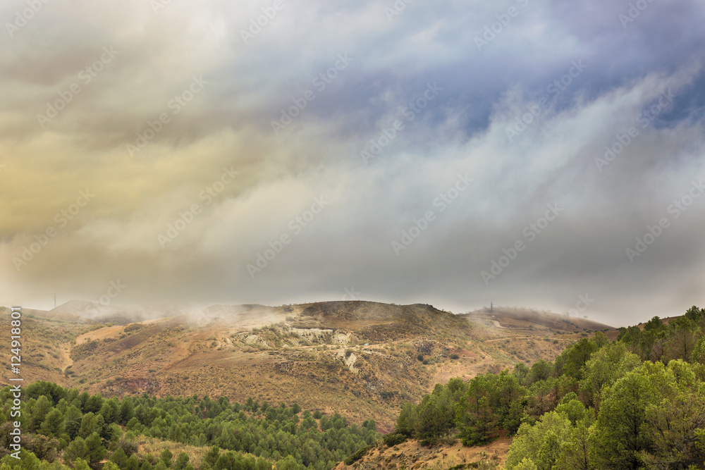 Mountainous landscape on a rainy sunset, with low clouds over the pines forest