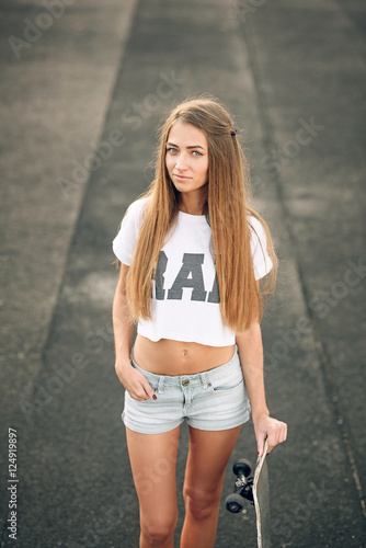 Cute beautiful teen girl with perfect body in a white T-shirt and short  shorts standing with skateboard in hand Stock Photo | Adobe Stock