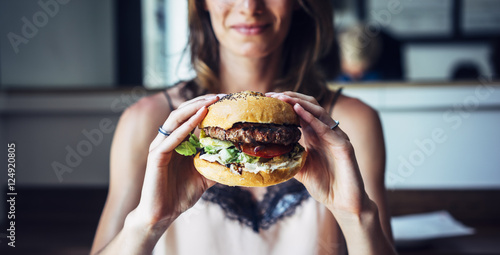 Young girl holding in female hands fast food burger  american unhealthy calories meal on background  mockup with copy space for text message or design  hungry person smiling with hamburger 