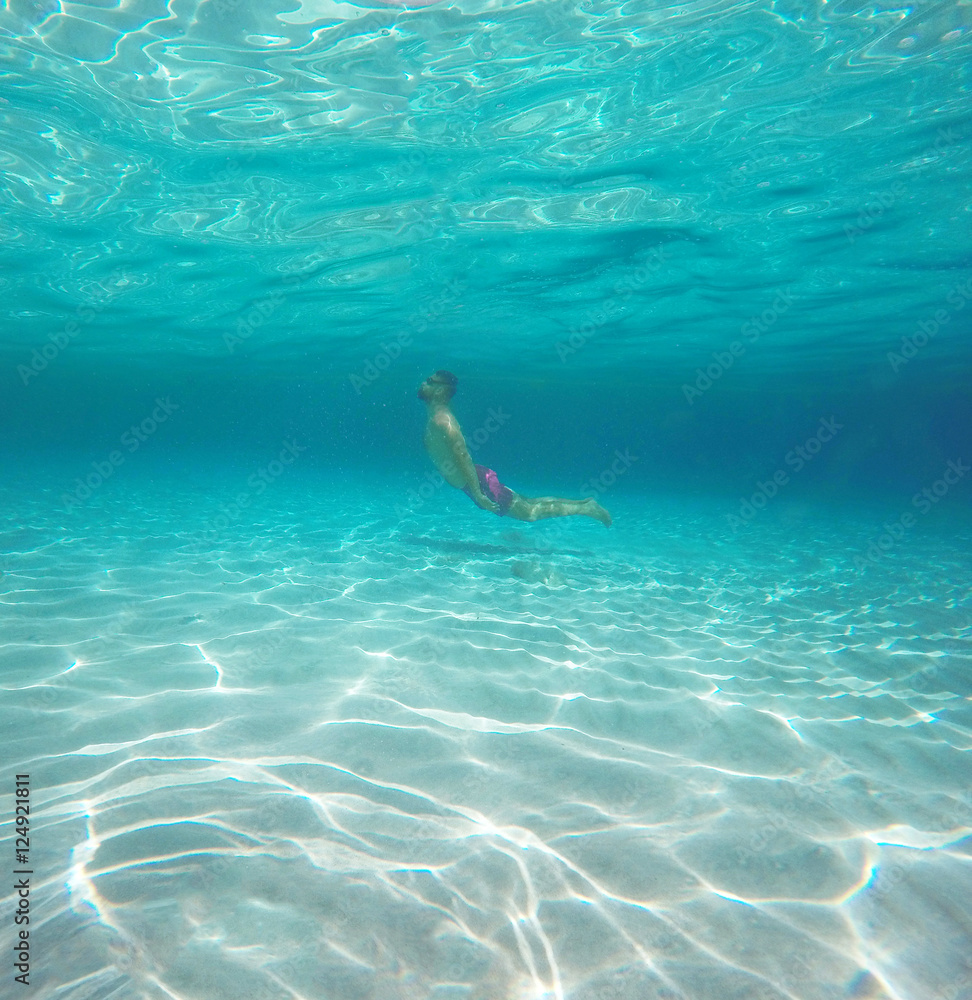 Man with glasses diving in a blue clean water of the sea