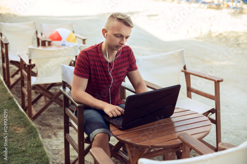 Young businessman.with headphones on a chair at the table using his laptop on the beach