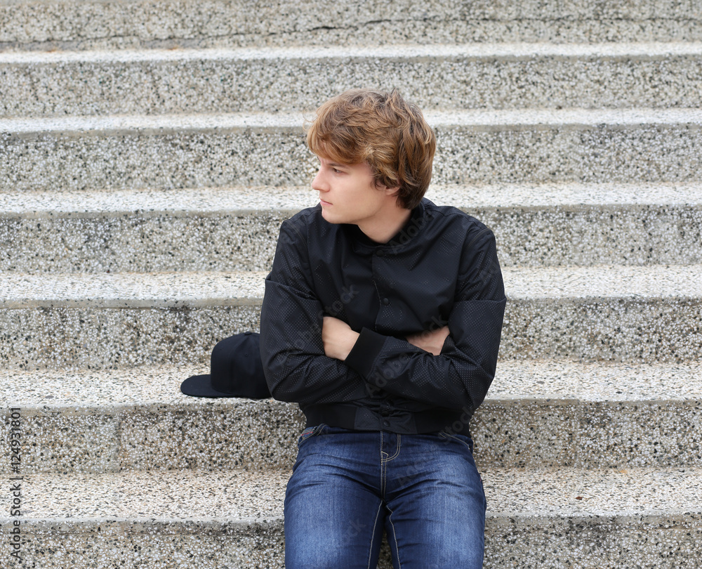 Portrait of attractive teenage boy sitting with crossed arms against grey background.