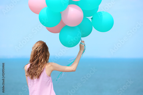 Beautiful young woman with colorful balloons on sea front © Africa Studio