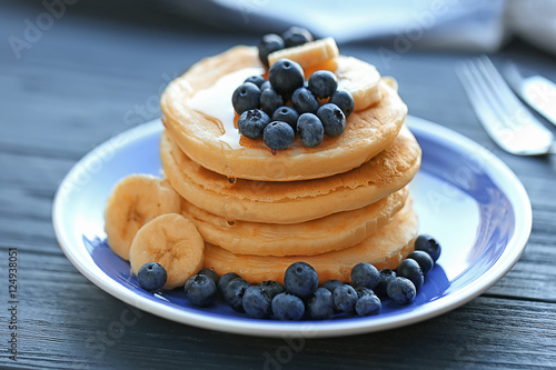 Plate with tasty pancakes, banana slices and berries on wooden table, close up view