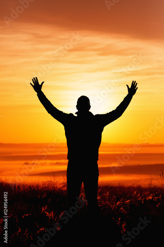 Silhouette of a man praying while facing the sun during Autumn
