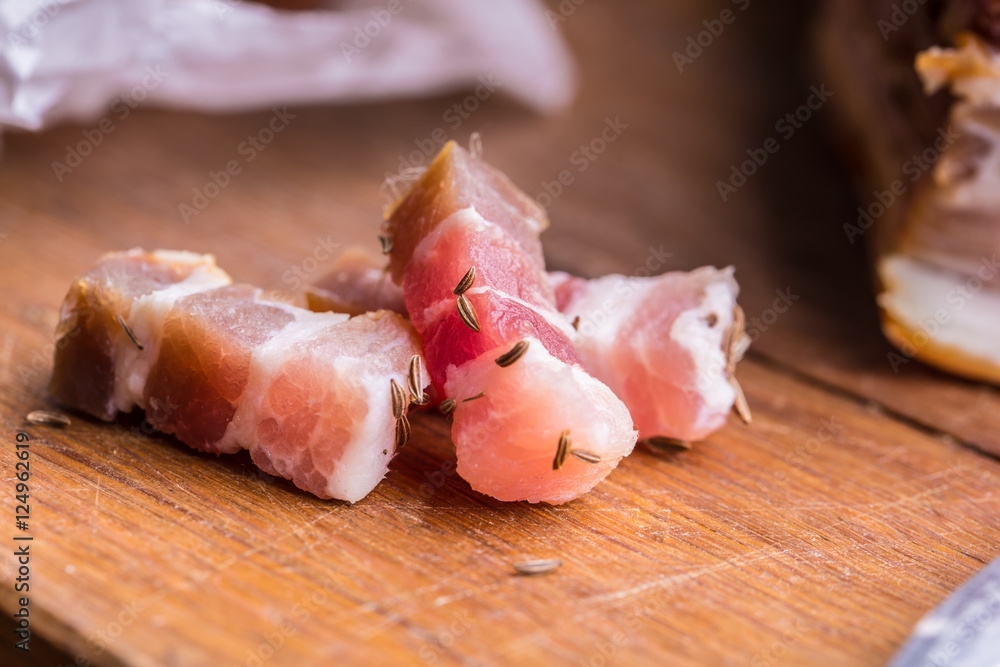 Raw smoked bacon slices on wooden board with cumin and herbs. Raw smoked bacon slices on wooden board with cumin and herbs.