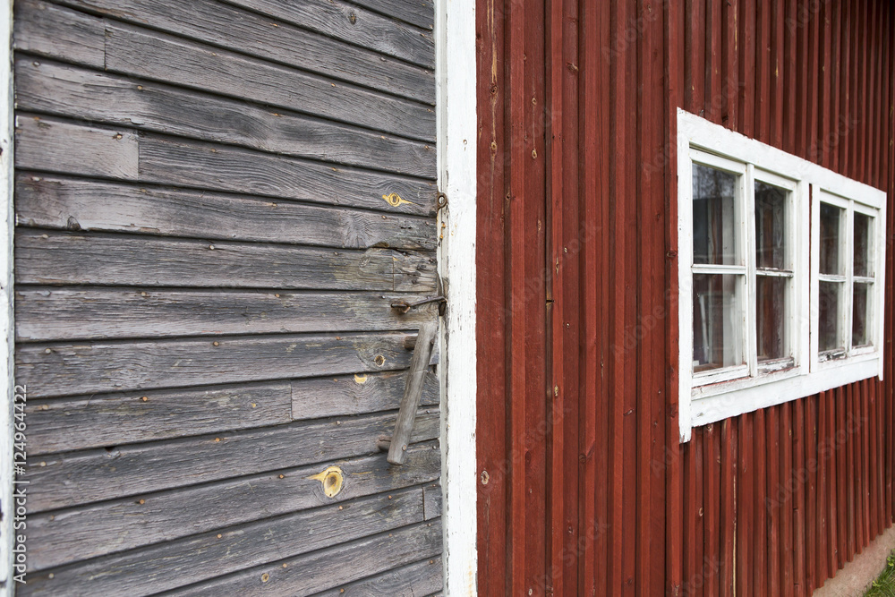 A wall of an old barn. Red shed walls with grey doors and white window frames.