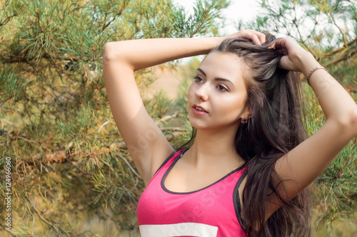 Young beautiful brunette model posing in the sports image of the park against the backdrop trees