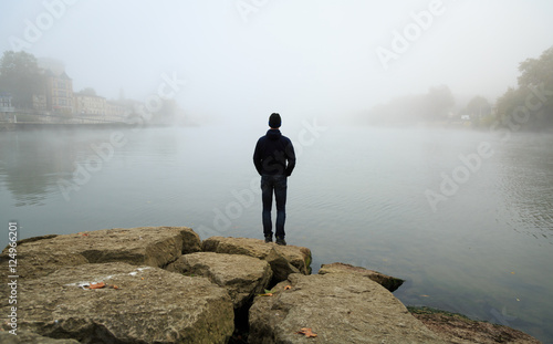 Man standing at the shore of the Saone and looking over the river during a foggy, autumn morning.