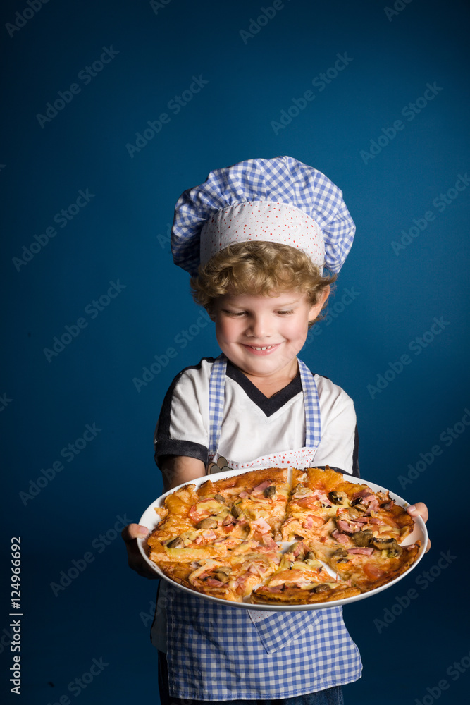 Little boy chef with a pizza on a blue background in studio Little boy chef with a pizza on a blue background in studio