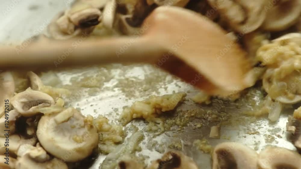 Close up of delicious sliced button mushrooms being stir-fried fried with onion and garlic, slow motion