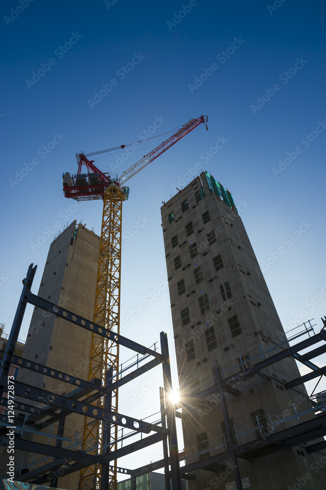 Modern hi-rise towers construction site backlit by morning sun under bright blue sky Modern hi-rise towers construction site backlit by morning sun under bright blue sky