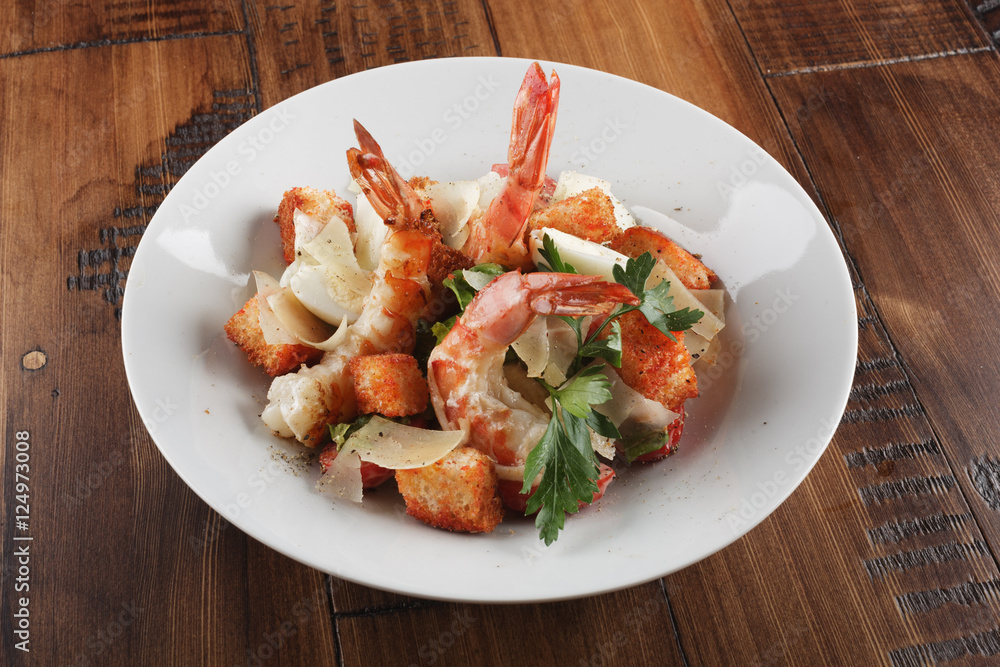 Caesar salad with king prawns in a white plate. Salad with shrimp on wooden brown background. Caesar salad with king prawns in a white plate. Salad with shrimp on wooden brown background.