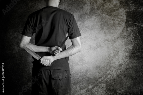 Close Up of a man holding knife behind back against black grunge