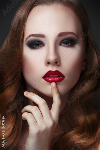 Fashion beauty portrait of gorgeous girl with curls and red lipstick in the style of Hollywood on a black background